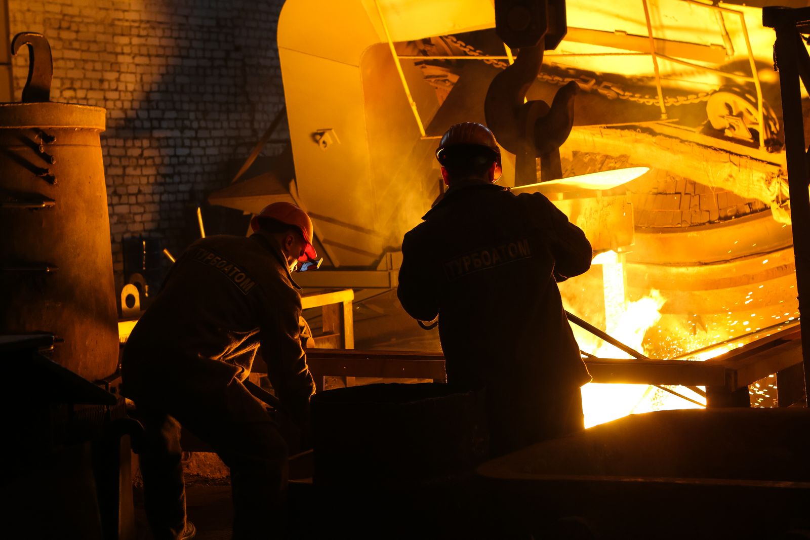Steelworkers beside a glowing furnace inside a steelmaking plant.