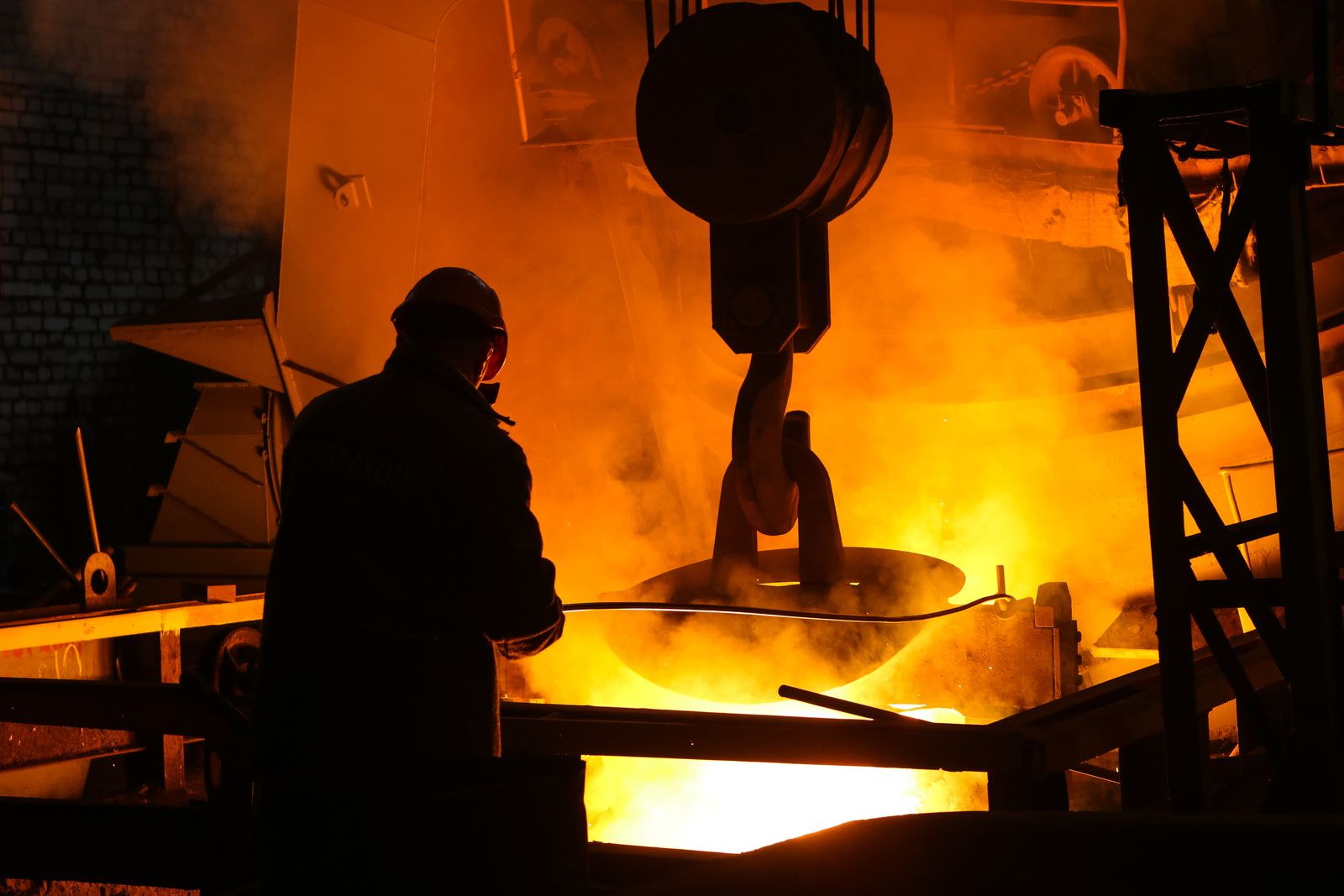 A worker silhouetted against a brightly lit steelmaking process.