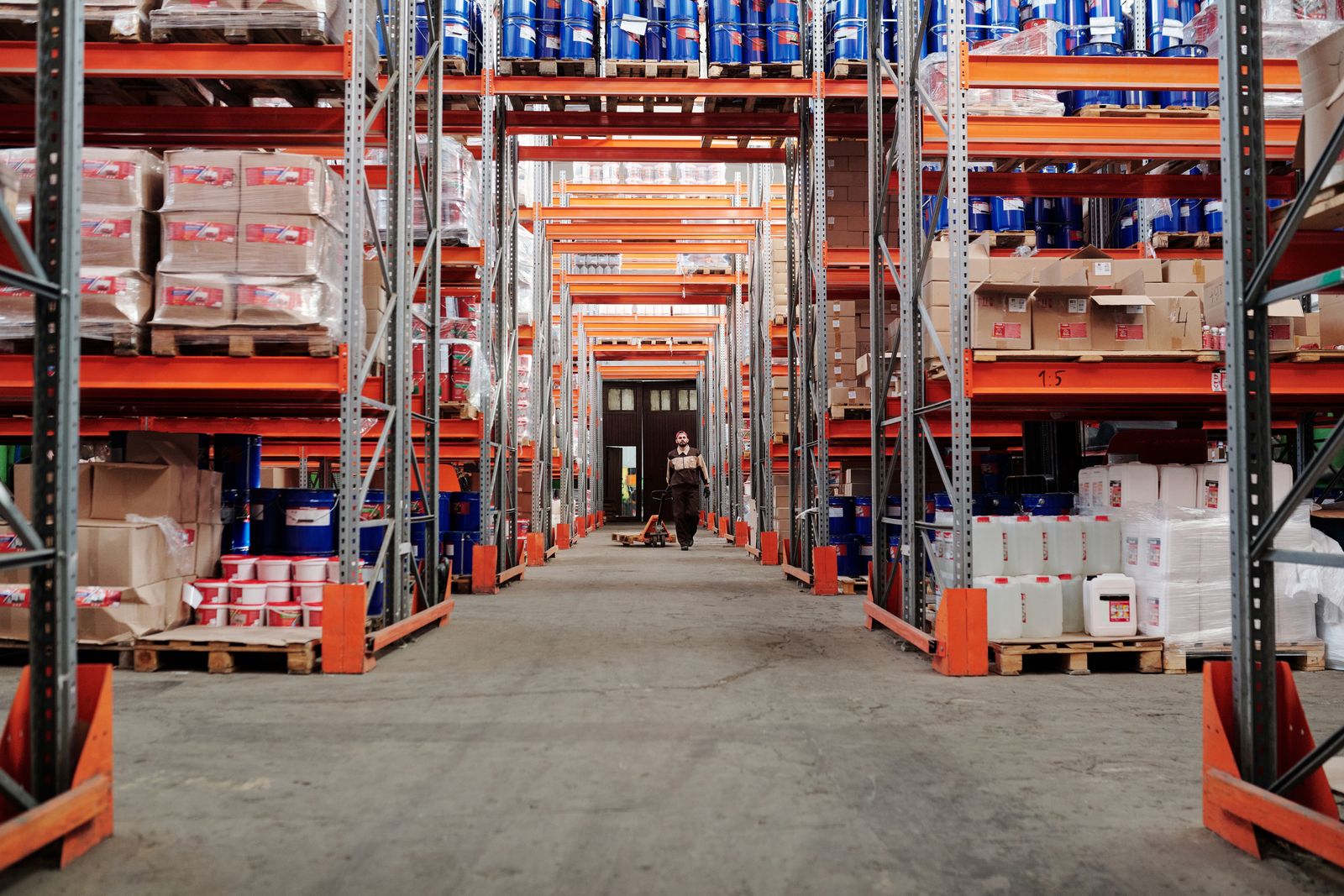 A warehouse aisle with high storage racks and a worker in the distance.